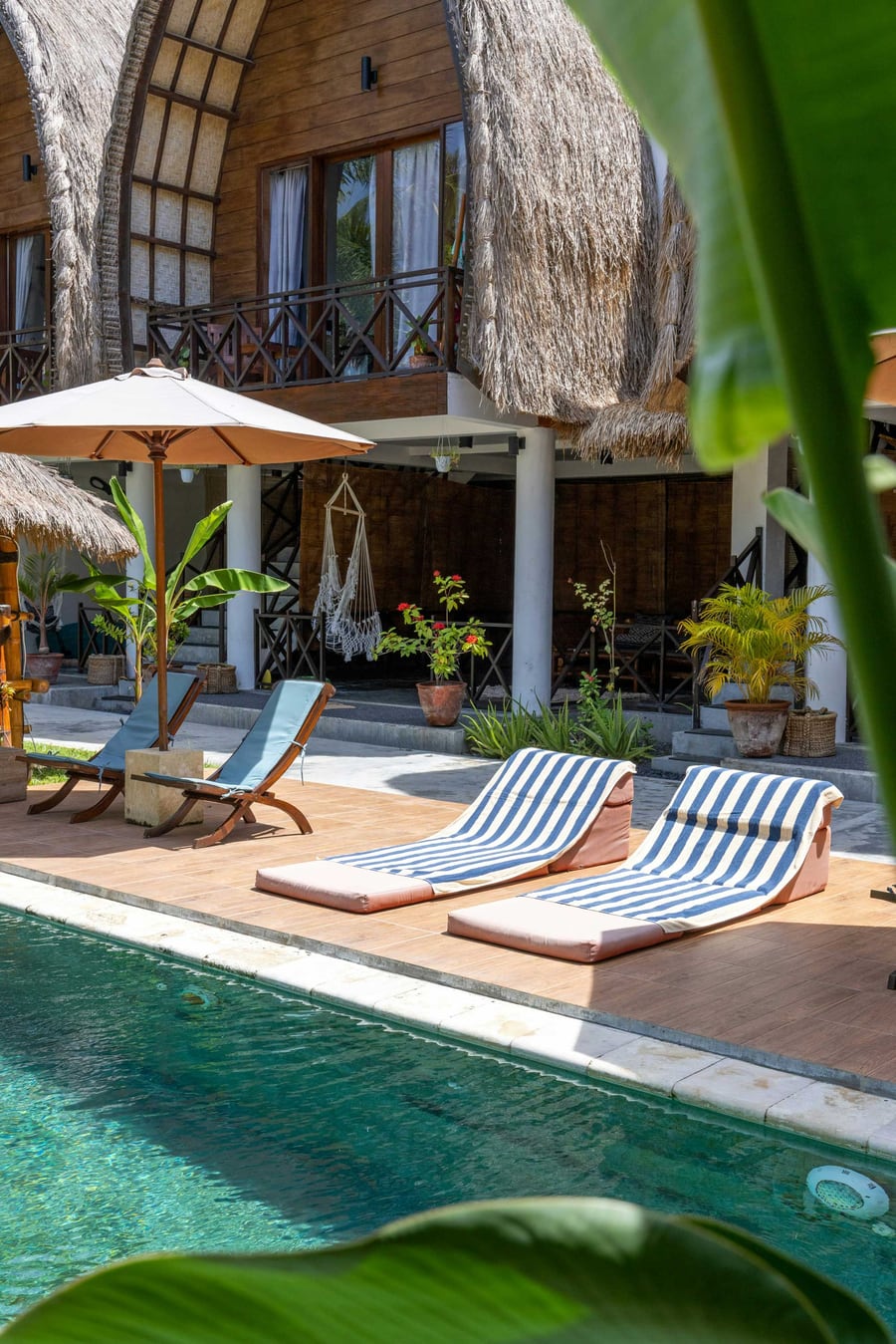 Striped sun loungers on a wooden deck beside a pool at a thatched villa