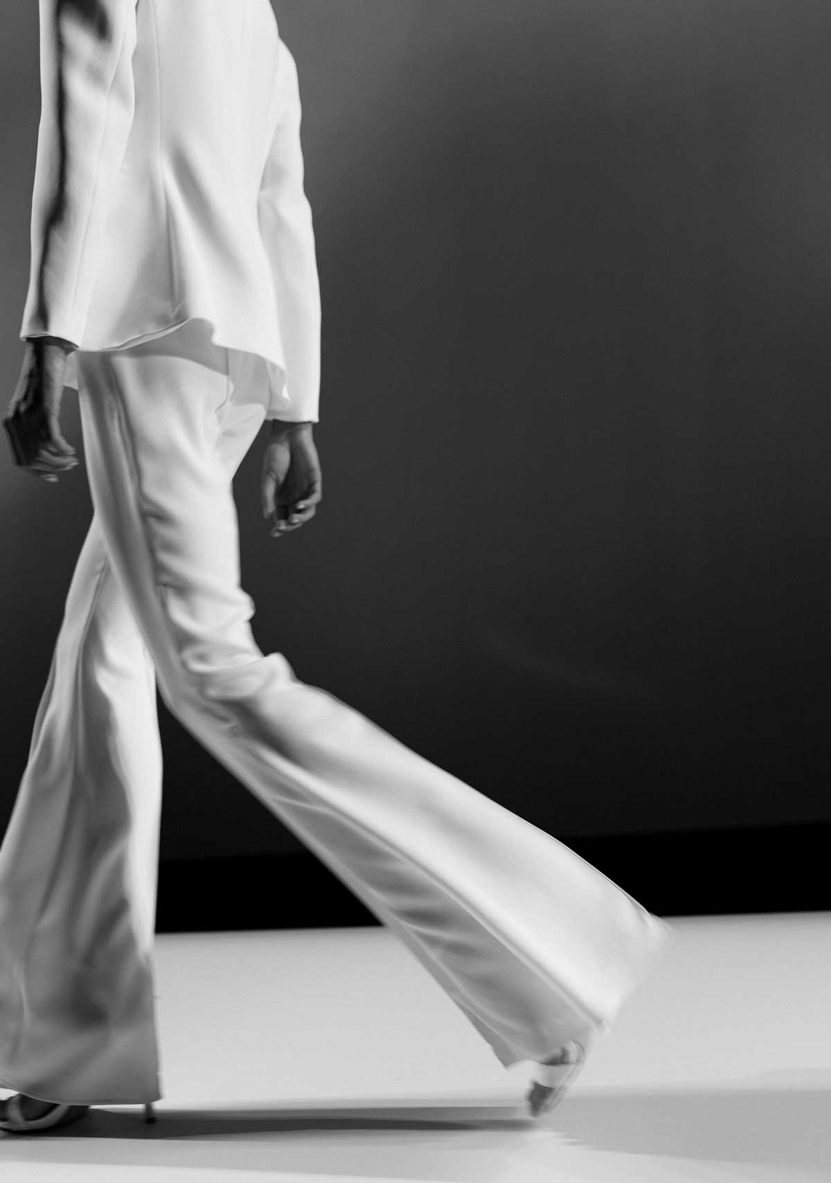 A model walking in a white satin trouser suit, photographed in black and white
